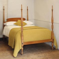 a bed with yellow sheets and pillows in a white room next to a wooden floor