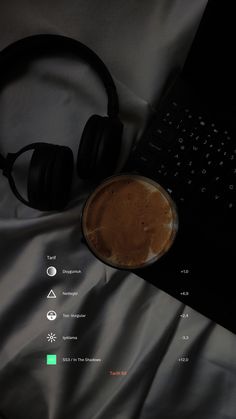 a laptop computer sitting on top of a bed next to headphones and a cup of coffee