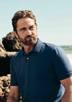 a man standing in front of some rocks on the beach with his hands in his pockets