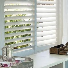 a window with white shutters and shoes on the table in front of it,