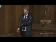 a man in a suit and tie is holding a remote control while standing next to a desk