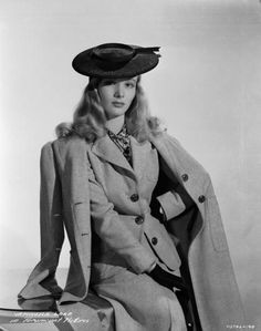 a woman wearing a coat and hat sitting on a chair