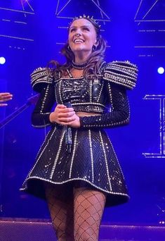 a woman in a black dress and fishnet stockings on stage with her arms crossed