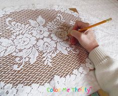 a person with a pencil in their hand on a white doily covered table cloth