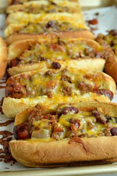 hot dogs in buns covered with chili and cheese on a baking sheet lined up