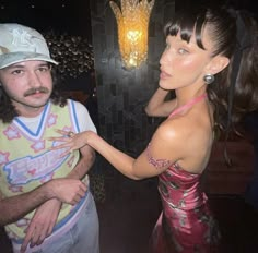 a man standing next to a woman in front of a lamp and wearing a hat