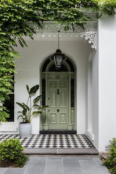 a green front door surrounded by greenery on a white house with black and white checkered flooring