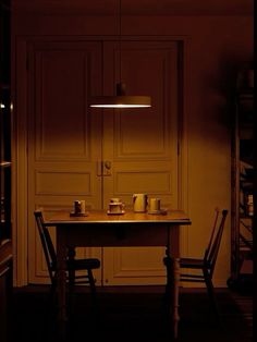 a table with two chairs and a lamp on it in a room that is dimly lit