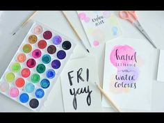 some watercolors are sitting on a table next to paper with words that say hand lettering