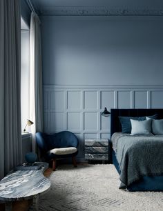 a bedroom with blue walls and carpeted flooring has a bed, chair, coffee table and ottoman