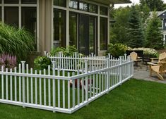 a white picket fence in front of a house with large windows and plants on the lawn