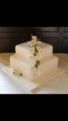 three tiered wedding cake with white flowers on the top and bottom, sitting on a table