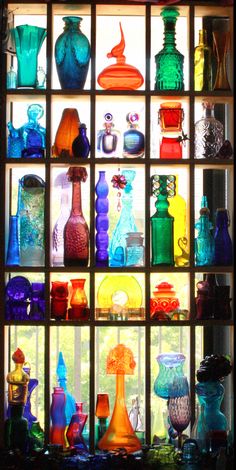 many different colored glass vases on display behind a window