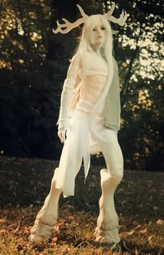 a woman dressed in white is walking through the grass with her hands on her hips