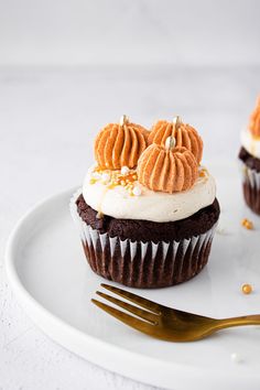 two cupcakes with white frosting and orange decorations on a plate next to a fork