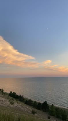 the sun is setting over the ocean with clouds in the sky and grass on the ground