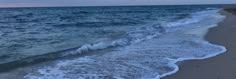 the ocean waves are coming in to shore on a beach at sunset or dawn with an overcast sky