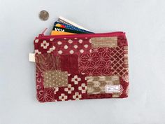 a red and beige patchwork wallet with a credit card holder next to it on a white surface