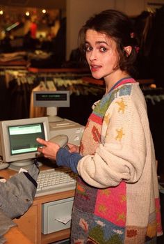 a woman is standing in front of a computer and looking at the screen with her finger