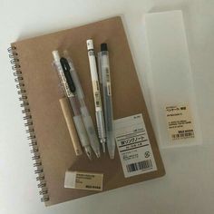 three pens and two erasers on top of a notebook