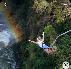 a woman flying through the air while riding a zip line next to a river and rainbow