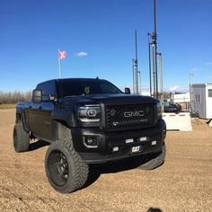 a black truck parked on top of a dirt field next to a trailer and flag pole