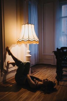 a woman laying on the floor next to a lamp in a room with wooden floors