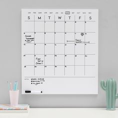 a whiteboard with a calendar on it next to a cactus