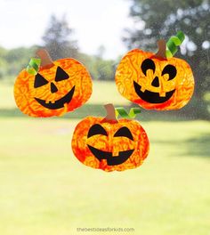 three paper pumpkins hanging from a window with green grass in the back ground and trees in the background