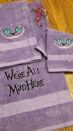 two purple towels with green eyes and the words we're all mad here on them