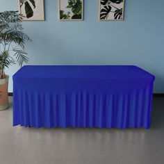 a blue table cloth draped over it in front of two potted plants and pictures on the wall