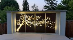 an outdoor area with a tree and lights on the wall, in front of a fence