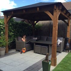 a woman sitting on a couch under a wooden pergolan in a backyard area