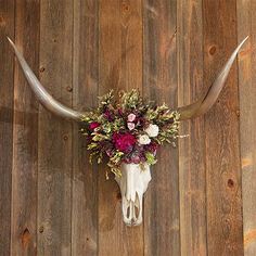 a cow skull with flowers and antlers on it's side against a wooden wall