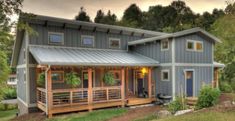 a large gray house sitting on top of a lush green hillside next to a forest