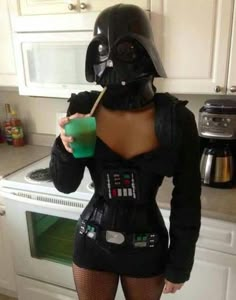 a woman dressed as darth vader drinking from a green cup in the kitchen