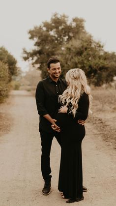 a pregnant couple walking down a dirt road