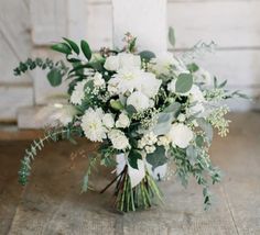 a bouquet of white flowers and greenery on a wooden floor in front of a door