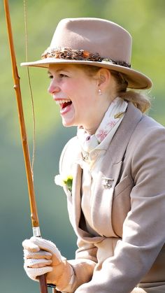 a woman in a hat and coat holding a fishing pole with her mouth wide open