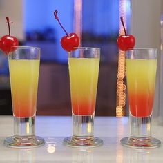 three glasses filled with drinks sitting on top of a counter