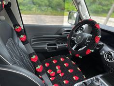 the steering wheel cover is decorated with strawberries on black fabric and sits in the driver's seat