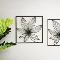 two metal wall art pieces mounted to the side of a white wall next to a potted plant