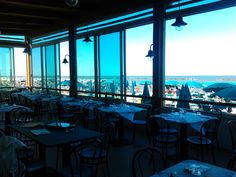 an empty restaurant with tables and umbrellas overlooking the ocean in front of large windows