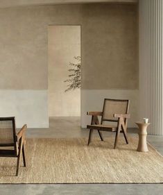 two chairs sitting on top of a rug in front of a wall with a vase