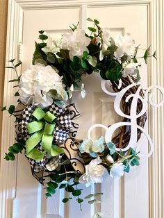 a wreath with white flowers and green ribbon hanging on the front door to welcome guests