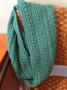 a green knitted scarf sitting on top of a wooden chair