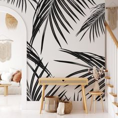 a white room with black and white palm leaves on the wall next to a wooden table