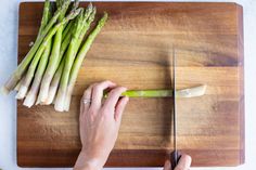 a person cutting asparagus on a wooden cutting board