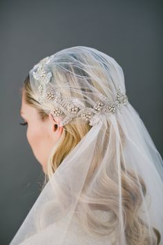 a woman wearing a veil and headpiece with flowers on it's side,