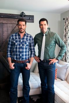 two men standing next to each other in front of a white couch and wooden door